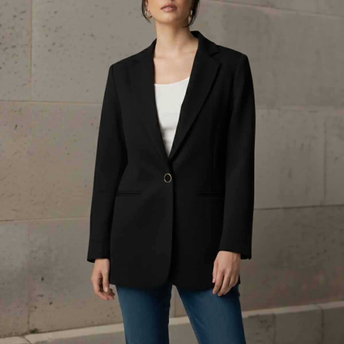 Woman wearing a black blazer and blue jeans against a stone wall.