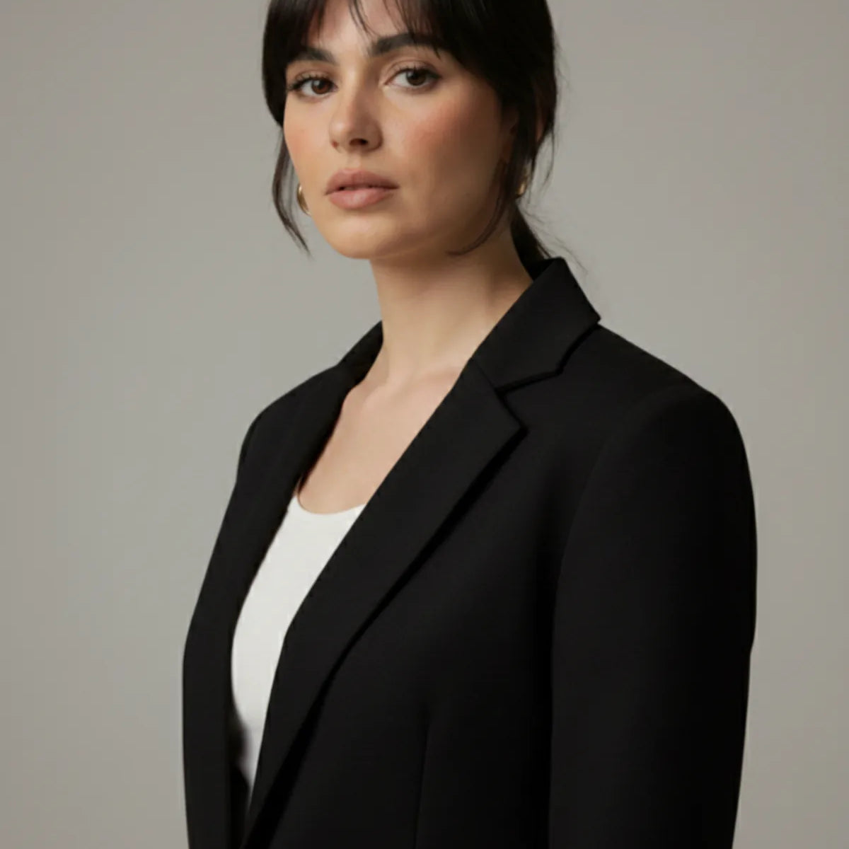 Woman wearing a black blazer over a white top against a neutral background