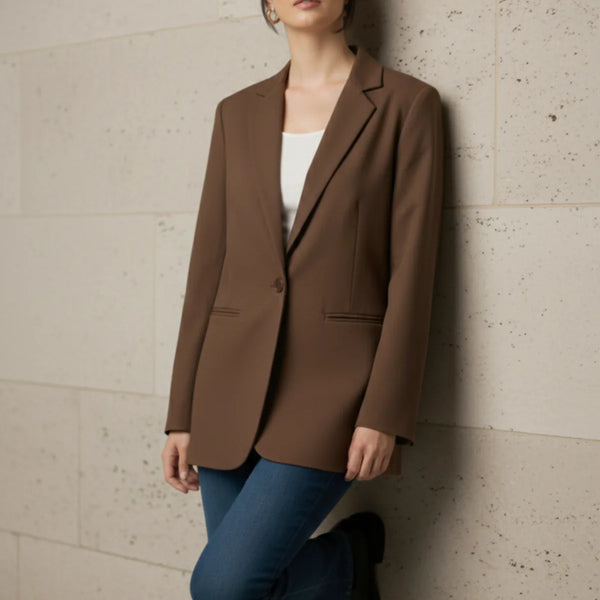 Woman wearing a mocha blazer and blue pants against a beige wall