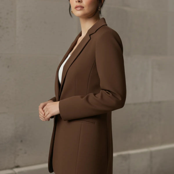 Woman wearing a mocha blazer and blue jeans against a stone wall.