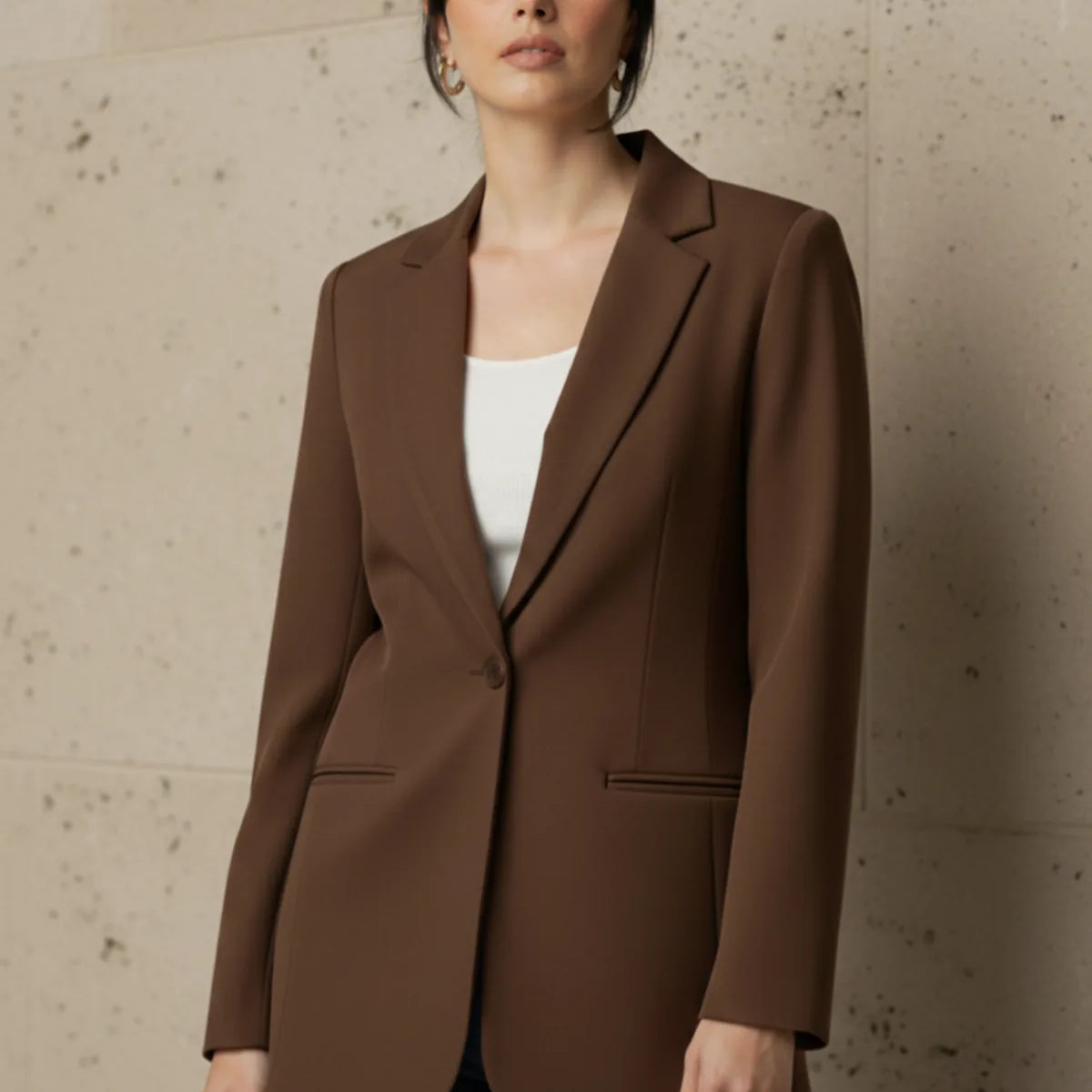 Woman wearing a mocha blazer against a beige wall