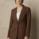 Woman wearing a mocha blazer against a beige wall