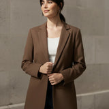 Woman wearing a mocha blazer against a stone wall.