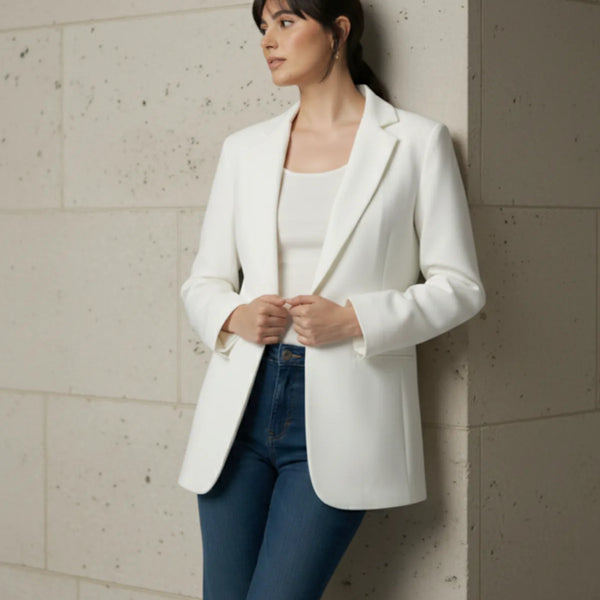 Woman wearing a white blazer and blue pants against a light-colored wall.