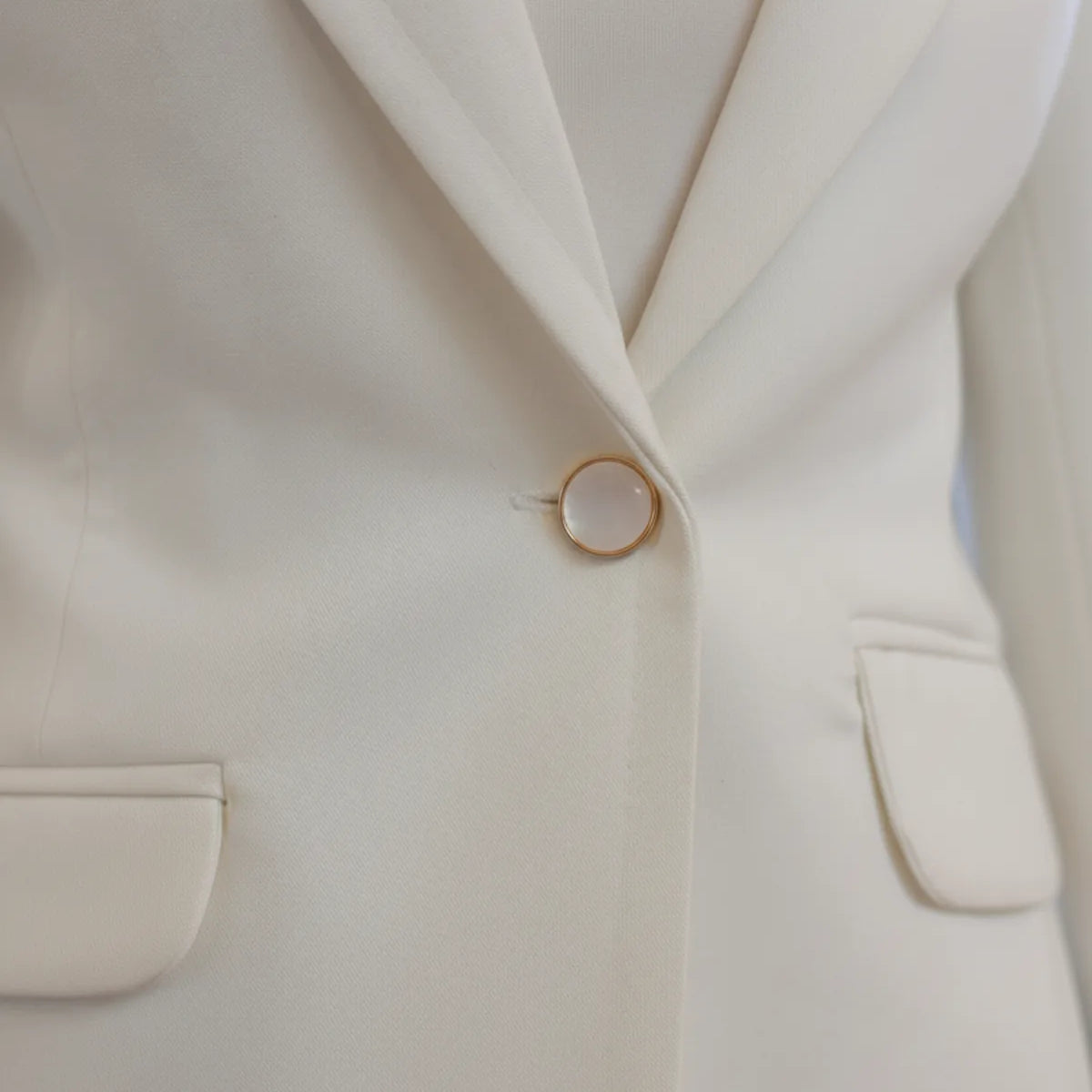 Close-up of a cream-colored blazer with a button and pocket details.