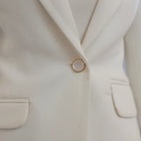 Close-up of a cream-colored blazer with a button and pocket details.