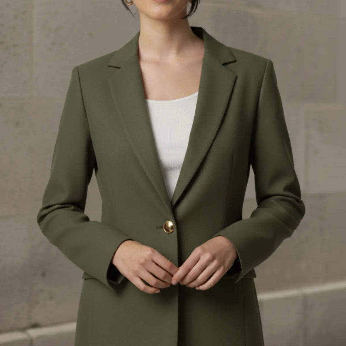 Woman wearing an olive blazer over a white top against a neutral background