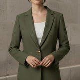 Woman wearing an olive blazer over a white top against a neutral background
