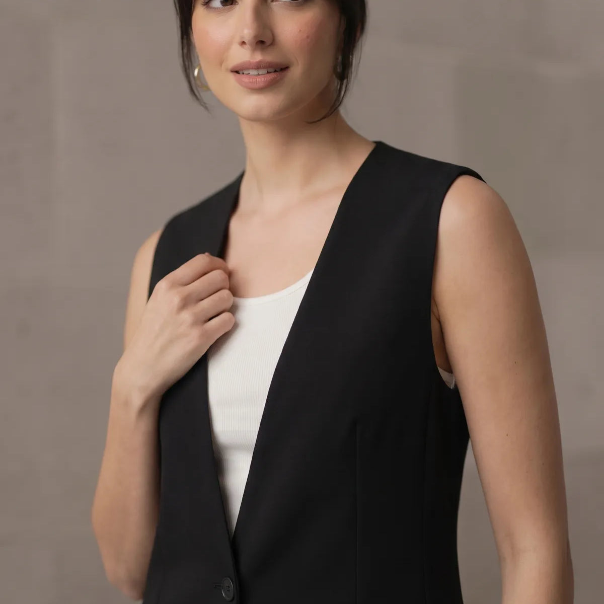 Close-up of a woman wearing a tailored black sleeveless blazer over a white top, highlighting the smooth lapel and shoulder fit.