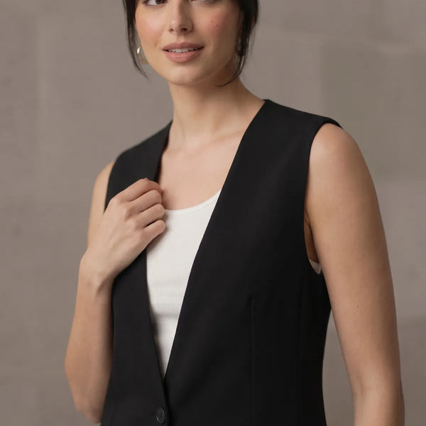 Close-up of a woman wearing a tailored black sleeveless blazer over a white top, highlighting the smooth lapel and shoulder fit.