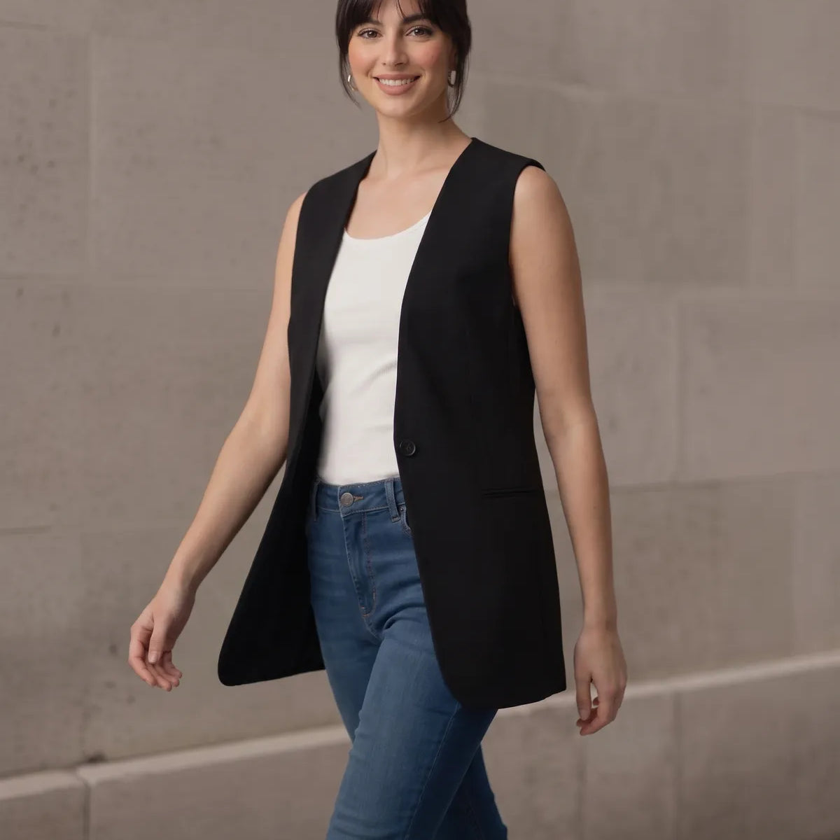 Woman walking confidently towards the camera in a stylish black sleeveless blazer, showcasing the garment's comfortable fit and movement.