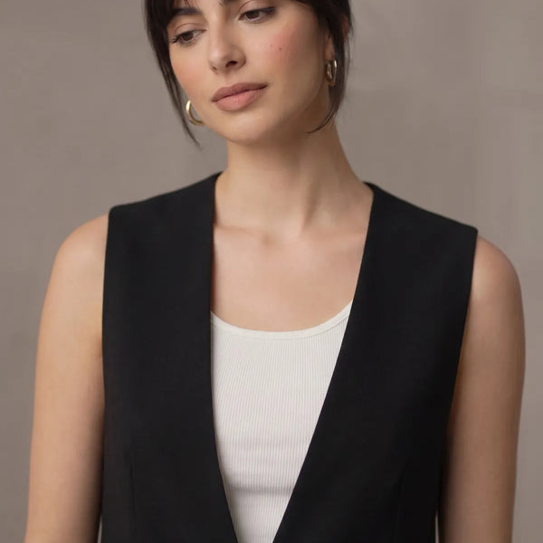 Portrait view of a woman modeling a black sleeveless tailored vest, focusing on the sleek V-neckline and upper body tailoring.