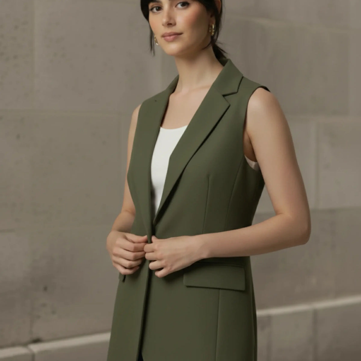 Three-quarter angle of a woman wearing an unbuttoned olive green longline vest over a white top, highlighting the garment's elegant drape and tailored fit.