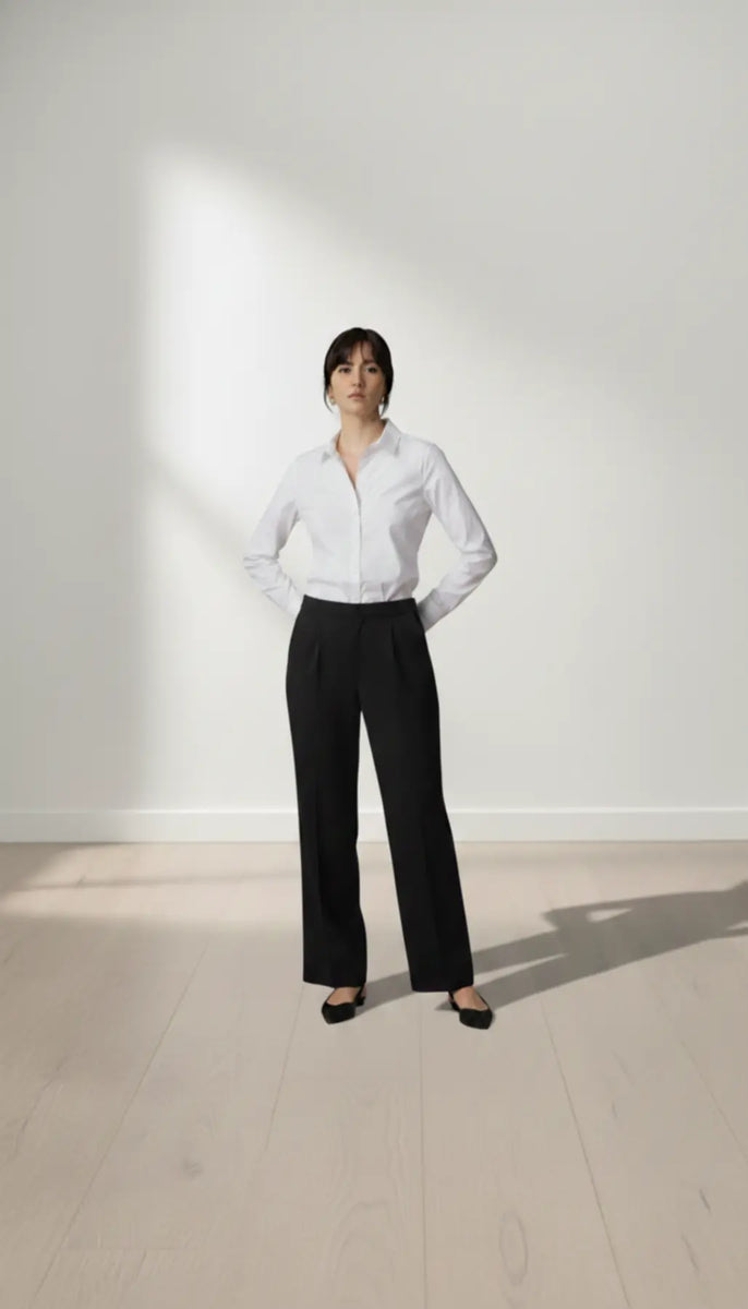Person wearing a white shirt and black trouser standing against a white wall.
