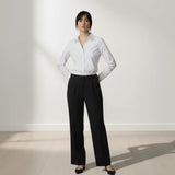 Person wearing a white shirt and black trouser standing against a white wall.