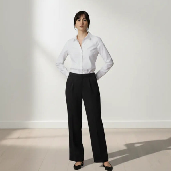 Person wearing a white shirt and black trouser standing against a white wall.