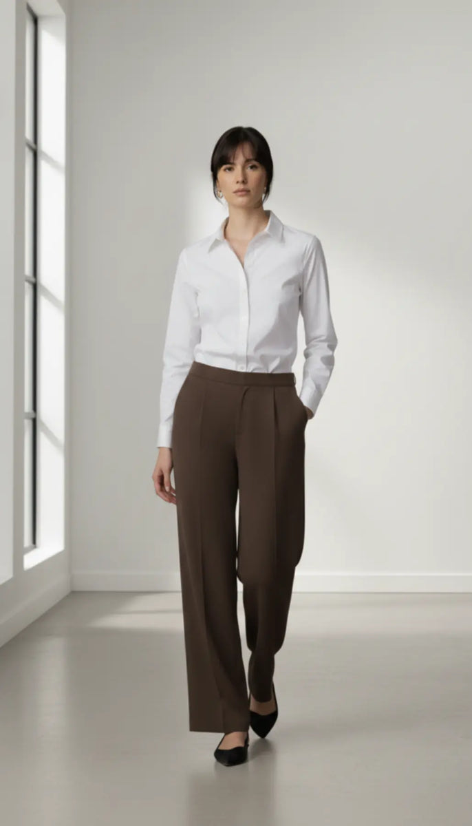 Woman wearing a white shirt and mocha trouser in a bright room.