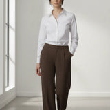 Woman wearing a white shirt and mocha trouser in a bright room.