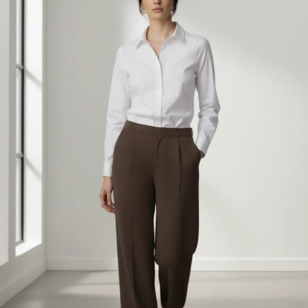 Woman wearing a white shirt and mocha trouser in a bright room.