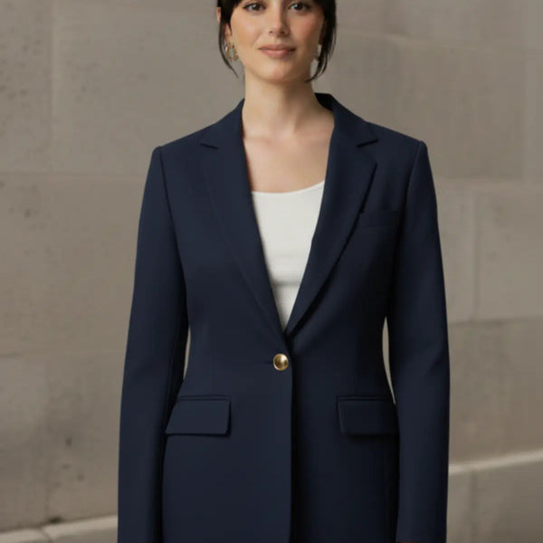 Woman wearing a navy blue suit with a white shirt against a beige wall.