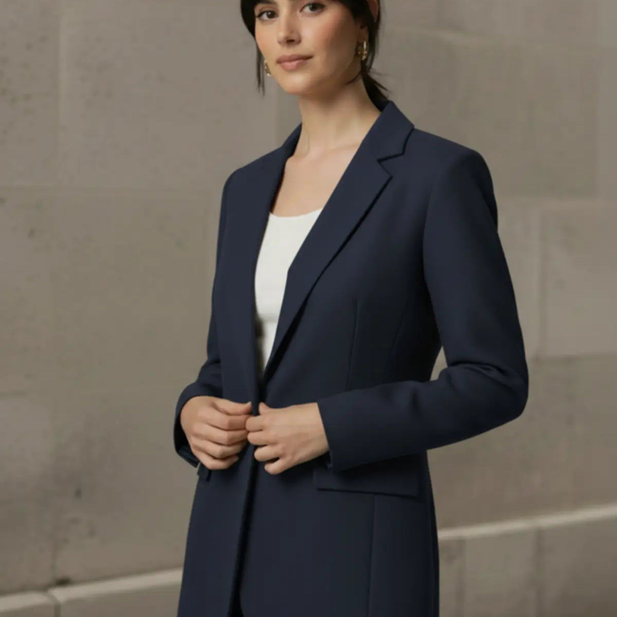 Woman wearing a navy blazer over a white shirt and blue jeans against a beige wall.