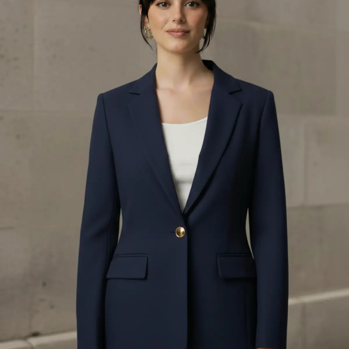 Woman wearing a navy blue blazer with a gold button against a neutral background