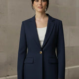 Woman wearing a navy blue blazer with a gold button against a neutral background