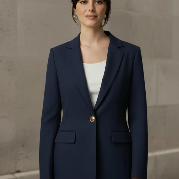Woman wearing a navy blue blazer with a gold button against a neutral background