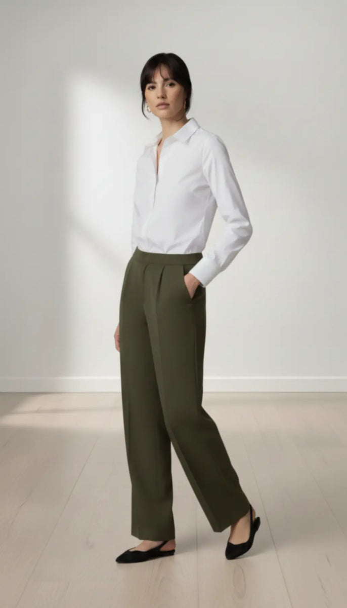 Woman wearing a white shirt and olive pants standing against a plain background