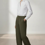 Woman wearing a white shirt and olive pants standing against a plain background