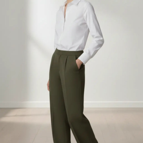 Woman wearing a white shirt and olive pants standing against a plain background