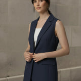 Woman adjusting a navy blue sleeveless blazer vest worn over a white tank top for professional office wear