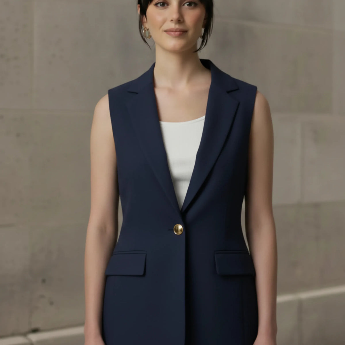 Woman modeling a tailored navy blue sleeveless blazer with a single gold button over a white top