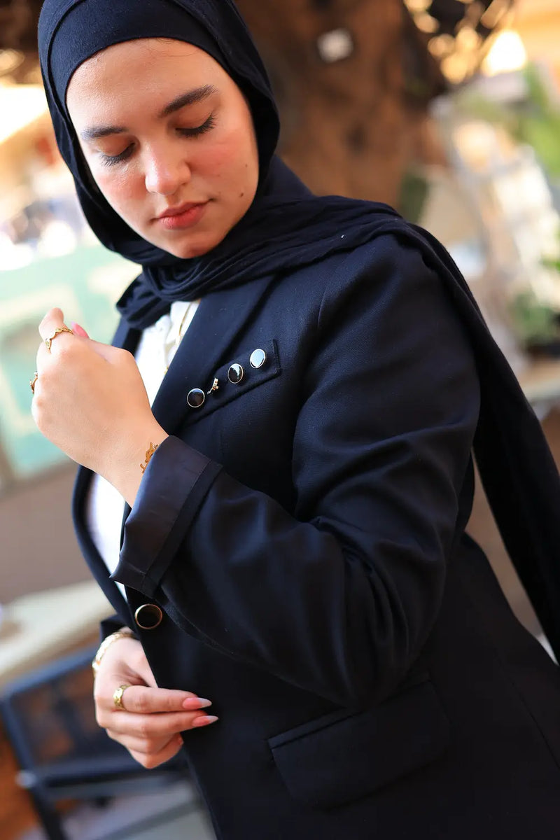 “ZAYTA Black tailored blazer on model wearing dark blue hijab, showing fabric and inner lining, outdoor setting”
