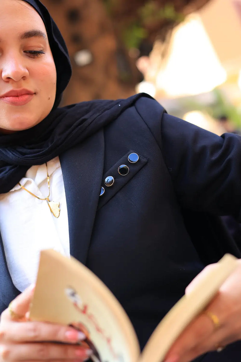 “ZAYTA black tailored blazer on model wearing hijab, showing fabric and inner lining, reading a book outdoors”

