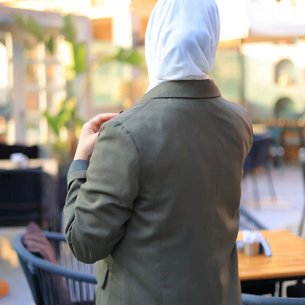 ZAYTA green tailored coat on model wearing white hijab, standing in an outdoor café setting, showing fit, fabric texture, and clean silhouette