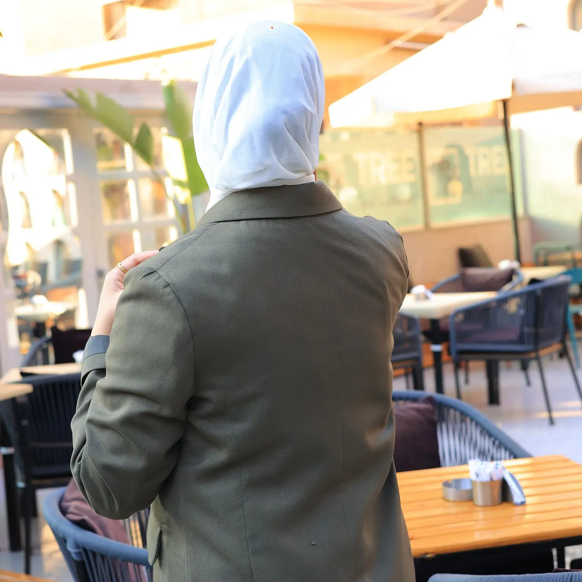 ZAYTA green tailored coat on model wearing white hijab, standing in an outdoor café setting, showing fit, details, and premium fabric