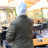 ZAYTA green tailored coat on model wearing white hijab, standing in an outdoor café setting, showing fit, details, and premium fabric