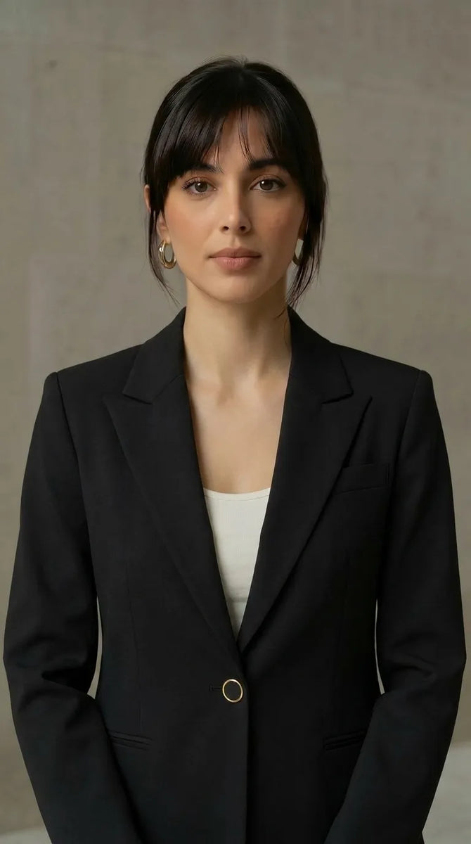 Woman wearing a black blazer over a white top against a neutral background