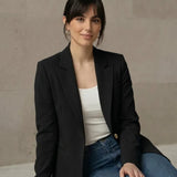 Woman wearing a black blazer and blue jeans sitting on a marble floor.