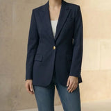 Woman wearing a navy blazer with gold buttons and blue jeans against a neutral background