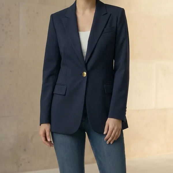 Woman wearing a navy blazer with gold buttons and blue jeans against a neutral background