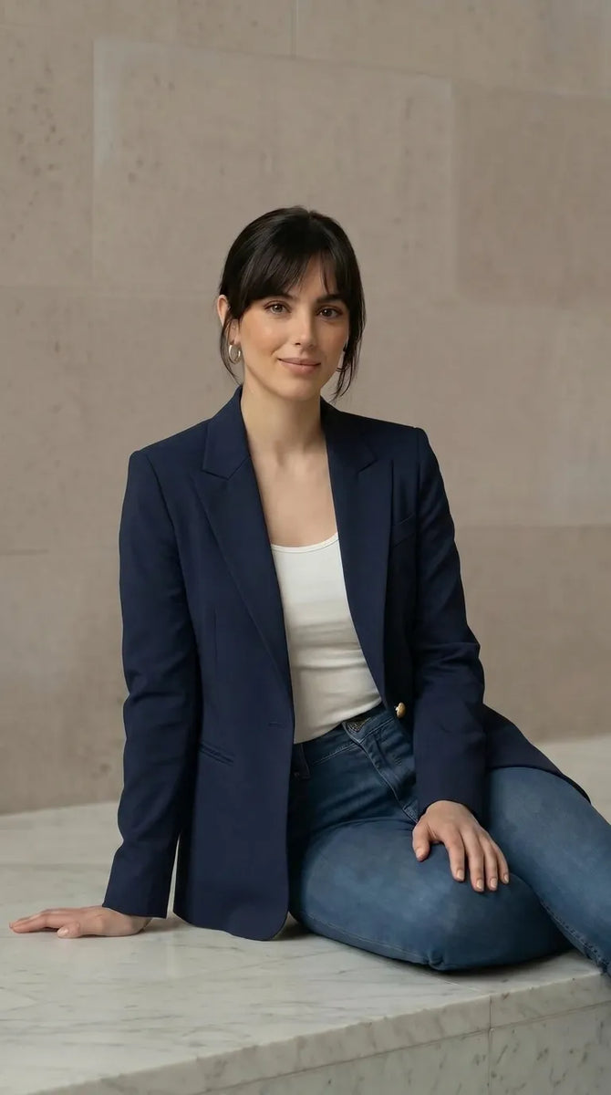 Woman wearing a navy blazer and jeans sitting on a marble ledge.