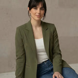 Woman wearing an olive blazer and blue jeans sitting on a marble ledge.