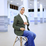 ZAYTA [color] tailored blazer on model, showing fabric and inner lining, sitting on a chair in modern indoor setting
