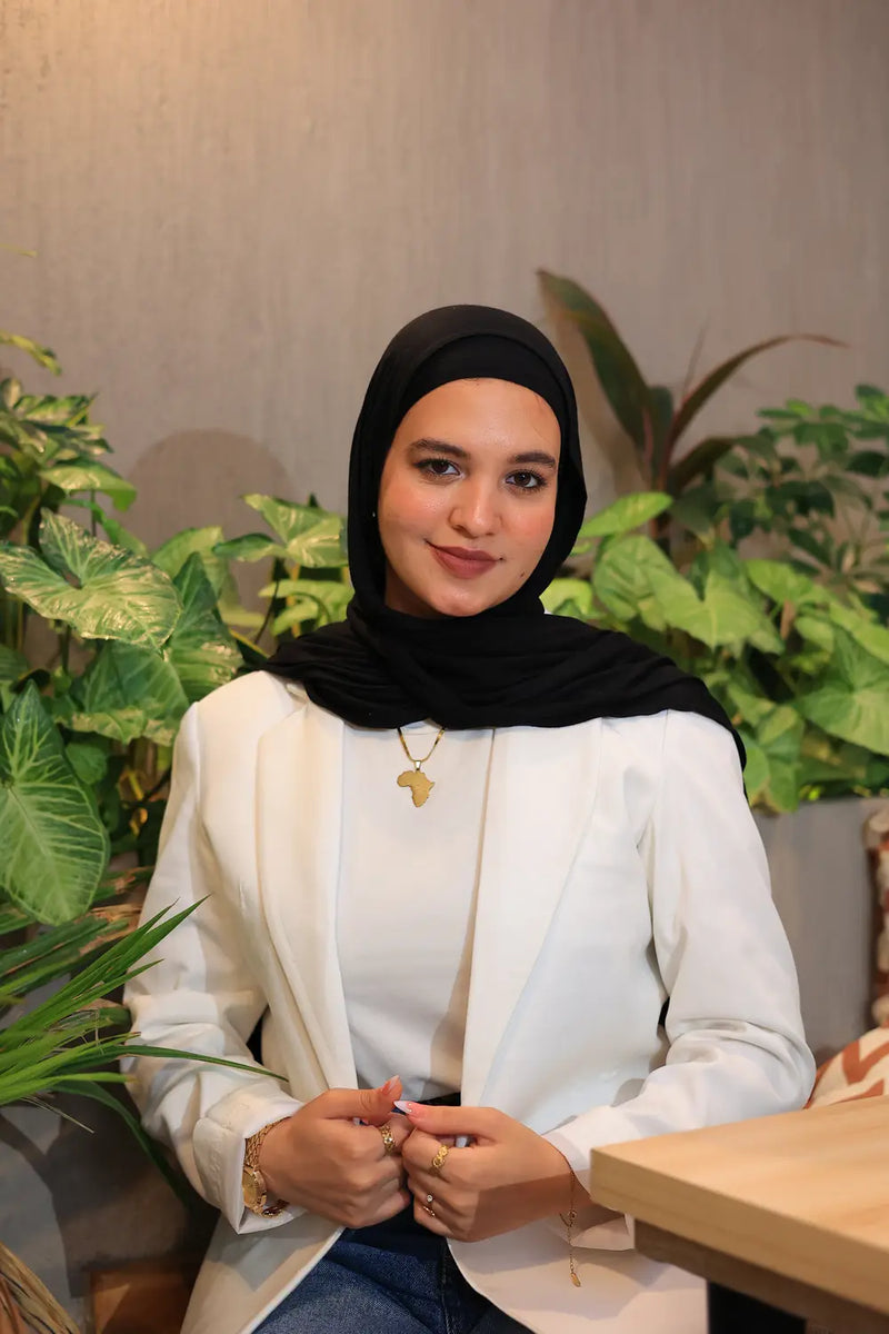 “ZAYTA off white women’s blazer on model wearing black hijab, tailored fit, sitting in a room with plants”