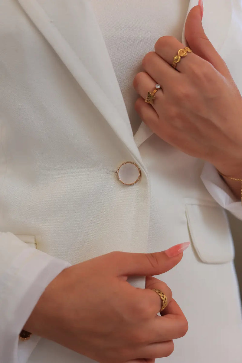 “Close-up of ZAYTA off white women’s blazer fabric and buttons, hands wearing gold rings”