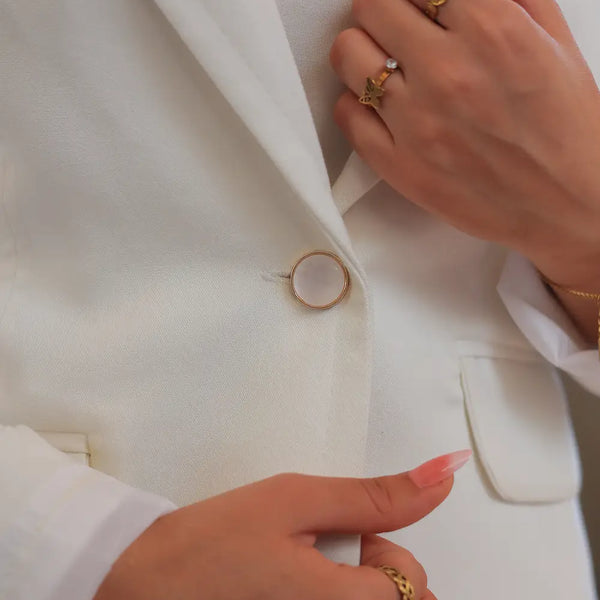 “Close-up of ZAYTA off white women’s blazer fabric and buttons, hands wearing gold rings”