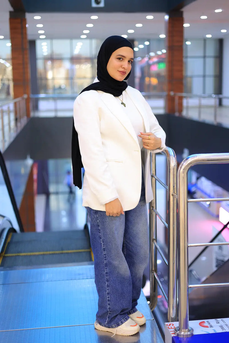 “ZAYTA off white women’s blazer on model paired with white sweater and blue jeans, modern indoor setting with escalators”
