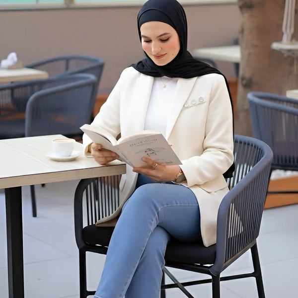 ZAYTA tailored blazer on model wearing hijab, showing fabric and inner lining, reading a book in modern cafe setting